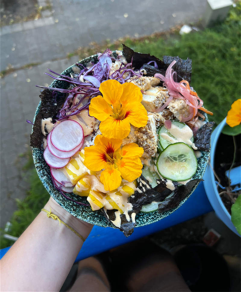 Vegan Pokebowl met veel kleurrijke groenten en twee grote eetbare bloemen, in een blauwe keramieke kom