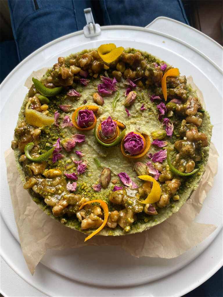 Vegan Glutenvrije pistachetaart gemaakt met avocado. Versierd met noten, rozen en citrusschillen