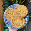 3 grote vegan chocolatechip cookies op een blauw keramieken bordje op een hand, van boven